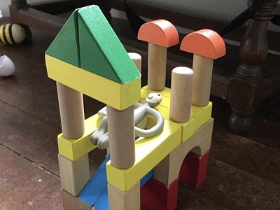 A teething toy monkey reclining on a building of toy wooden bricks of different colours and shapes